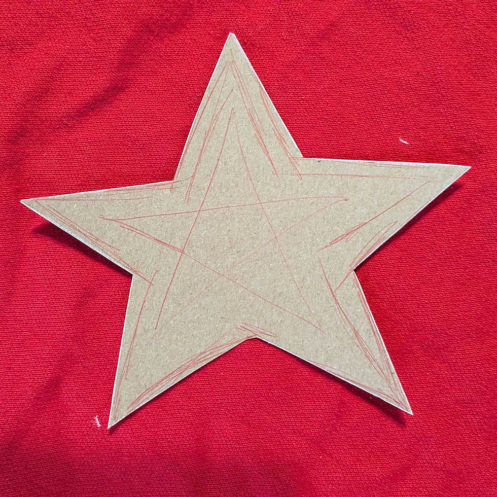 A cardboard star with red pencil sketches on a vibrant red fabric background. No text visible. Simple, artistic, and bright setting.