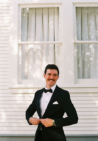 groom in a tuxedo in front of a white building