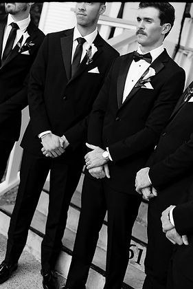 Groom and his groomsmen standing with their hands folded in front of a wedding venue
