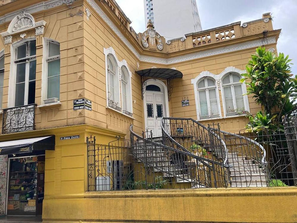 Fachada do casarão histórico ocre na esquina da Praça Osório com a Travessa Jesuíno Marcondes em Curitiba. Em destaque, a escadaria externa dupla de ferro forjado que leva à porta principal branca de estilo eclético.