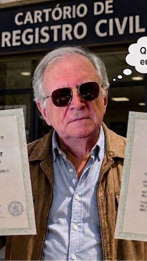 otografia digital mostrando um homem idoso de cabelos grisalhos e óculos escuros, vestindo uma jaqueta marrom, posicionado em frente ao letreiro "Cartório de Registro Civil". Ele segura duas certidões de nascimento: uma em nome de Caio Júlio César Brandão Pinto e outra em nome de Caio Júlio César Lopes Cançado. Um balão de pensamento sai de sua cabeça com a frase "Quem sou eu, afinal?".