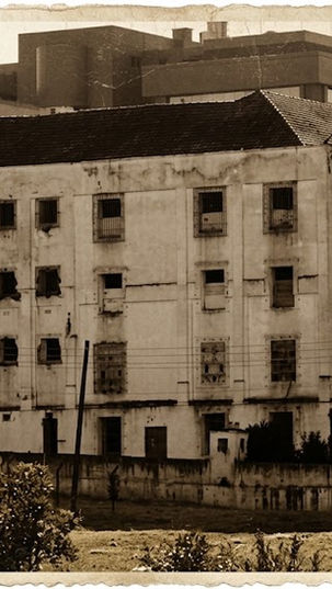 Fachada histórica do antigo Presídio do Ahú, em Curitiba, em fotografia com efeito envelhecido em tom sépia, exibindo paredes desgastadas e janelas com grades.