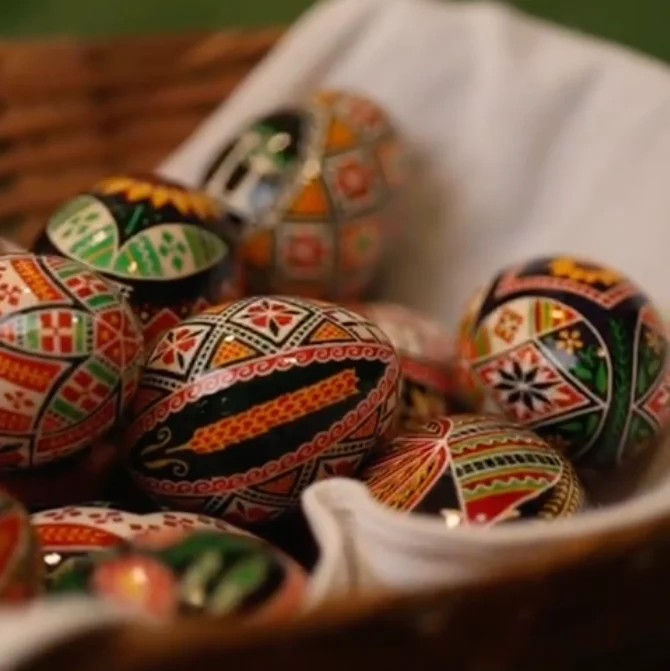 Cesto com diversas pêssankas ucranianas artesanais, exibindo desenhos geométricos detalhados e cores vibrantes como vermelho, amarelo, preto e verde.