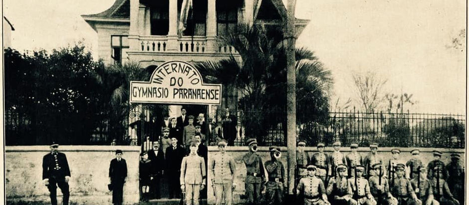 Fotografia histórica em tom sépia da fachada do imponente edifício do antigo Gymnásio Paranaense em Curitiba, destacando sua arquitetura clássica do início do século XX.