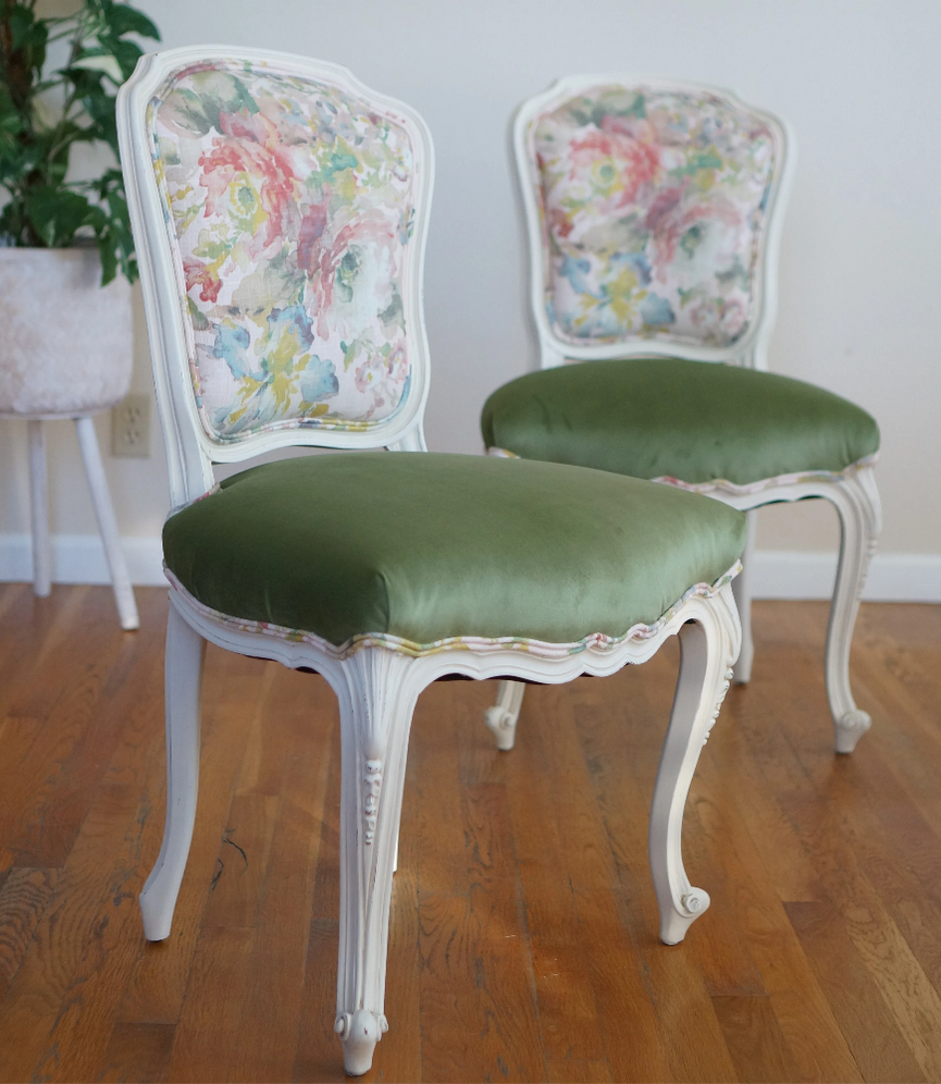 A pair of French chairs with floral piping, green velvet seats, and checkered backs. The frames are a soft cream color.