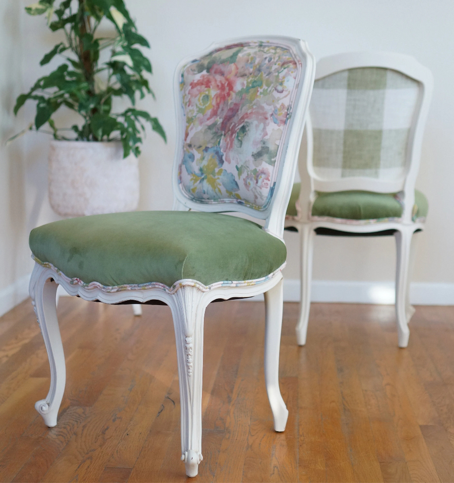 A pair of French chairs with floral piping, green velvet seats, and checkered backs. The frames are a soft cream color.