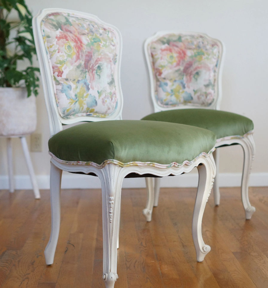 A pair of French chairs with floral piping, green velvet seats, and checkered backs. The frames are a soft cream color.