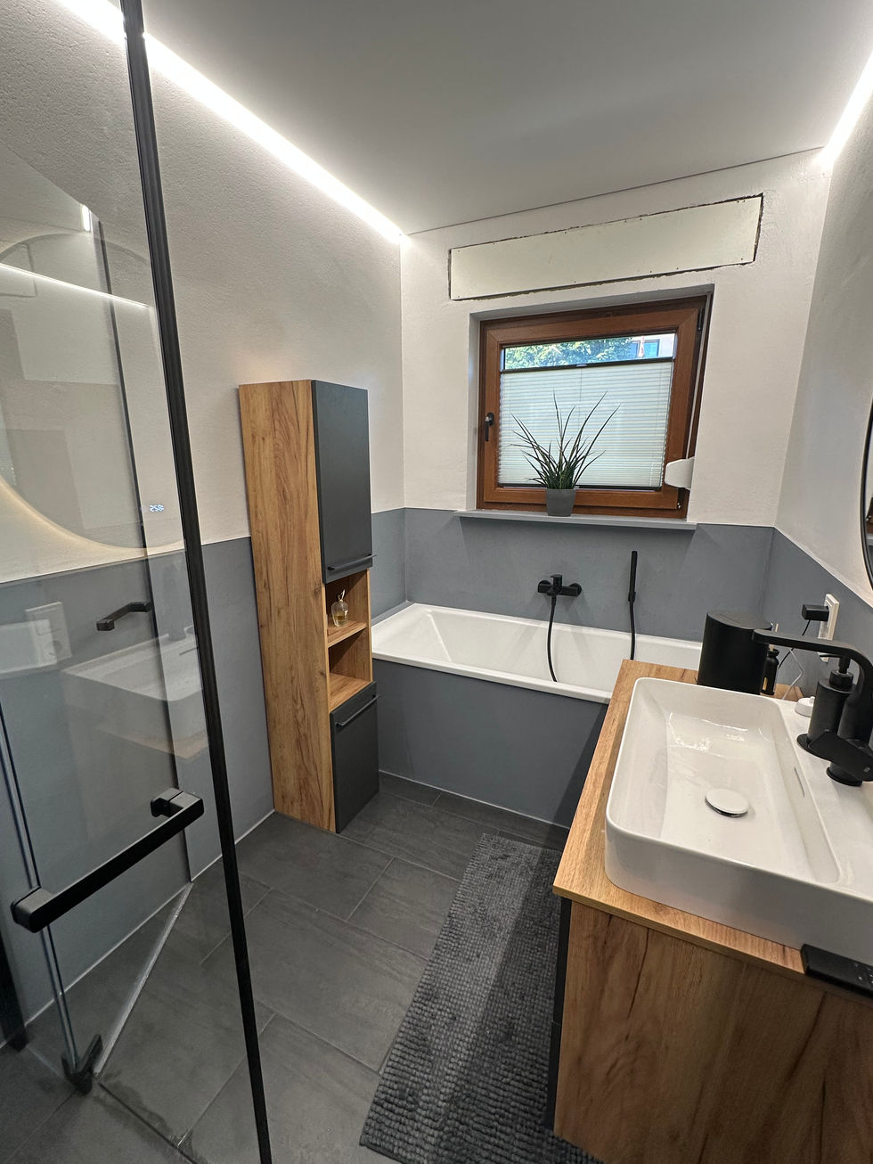 Detailansicht des hinteren Raumes zum Fenster hin, Badewanne und fugenlose Oberflächen sowie seitliche Ansicht Waschbecken und Waschbeckenunterschrank