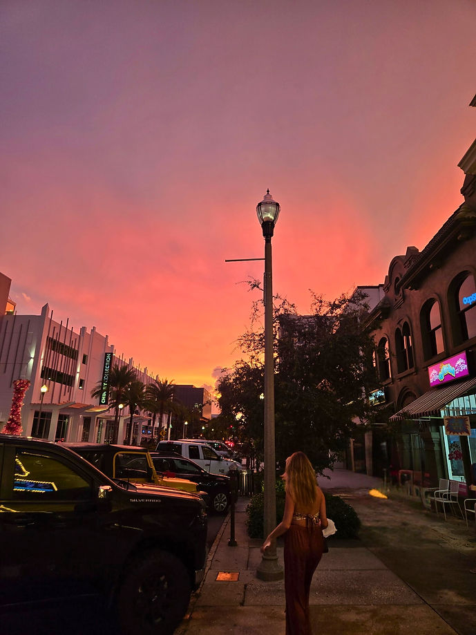 A woman walking down a city street at dusk under a pink-orange sky symbolizing an intentional pause - part healing, part building, between the next chapter of travel and life.
