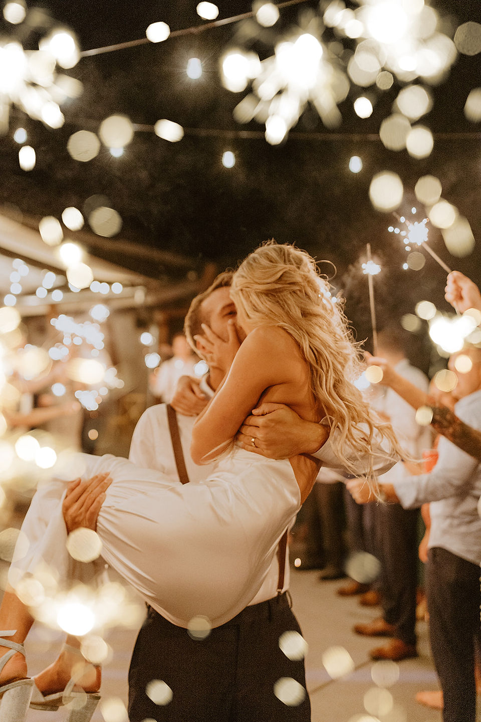groom carries bride through sparklers