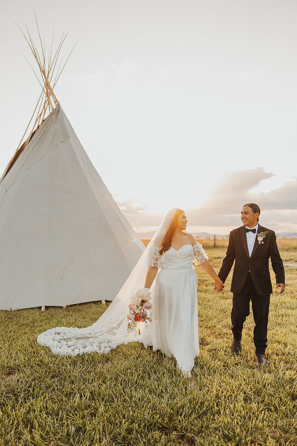 bride and groom walking during sunset by a teepee