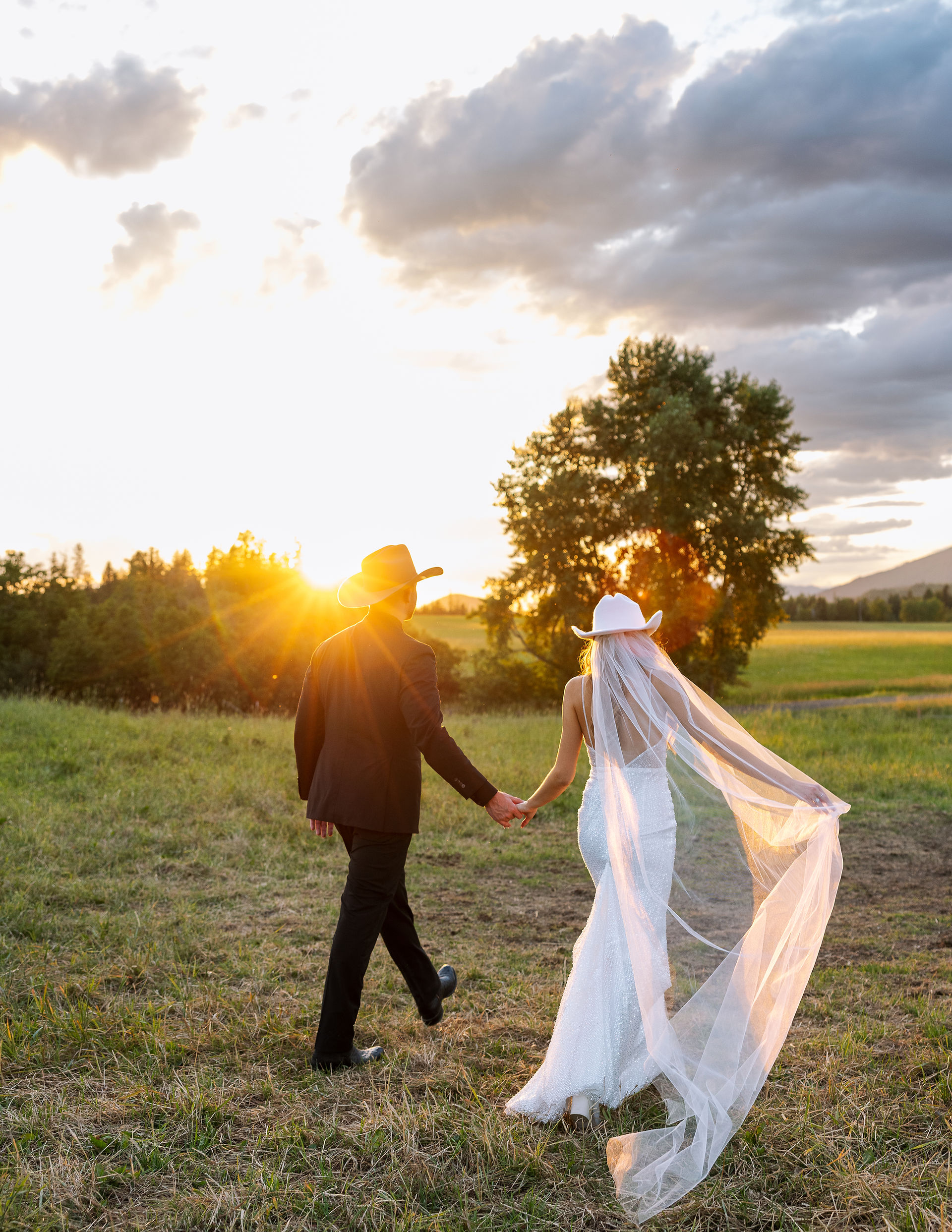 bride and groom with cowboy hats walking at sunset