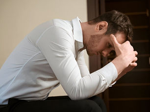 A man in a white shirt sitting with his head in his hands, depicting the heavy weight of existential dread and intrusive thoughts treated at BFF Clinic.
