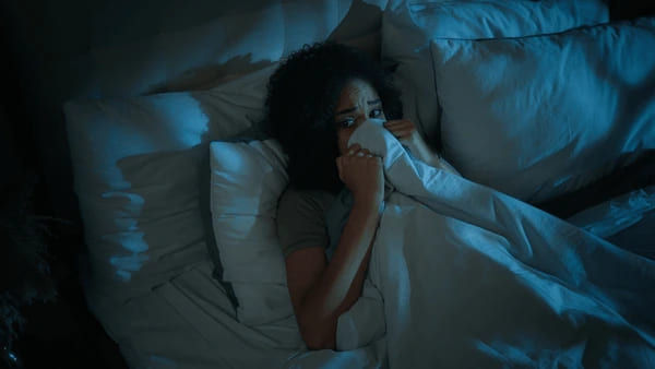 Woman with dark hair experiencing somniphobia symptoms, looking terrified while clutching the duvet in bed at night. This image illustrates the intense fear of sleep treated at BFF Clinic in New Smyrna Beach, South Daytona, and Deland, FL.