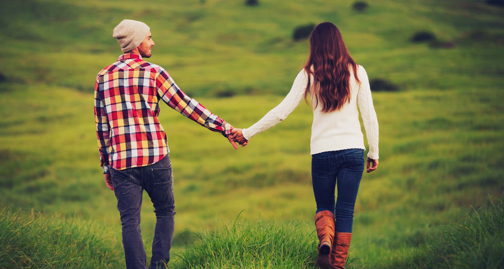 Coppia che si tiene per mano, passeggiata romantica in un campo