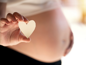 Close-up of a pregnant woman holding a small paper heart in front of her bare belly, symbolizing love and care during pregnancy.