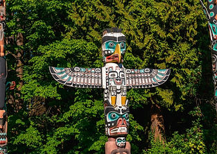 Carved totem pole with bird and animal figures against green trees