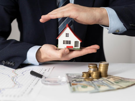 A professional protecting a model house with hands beside coins and cash, representing reverse mortgage and home equity planning in Canada.