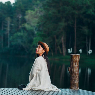 A woman sitting near the water and nature, experiencing silence and exploring deep self. 