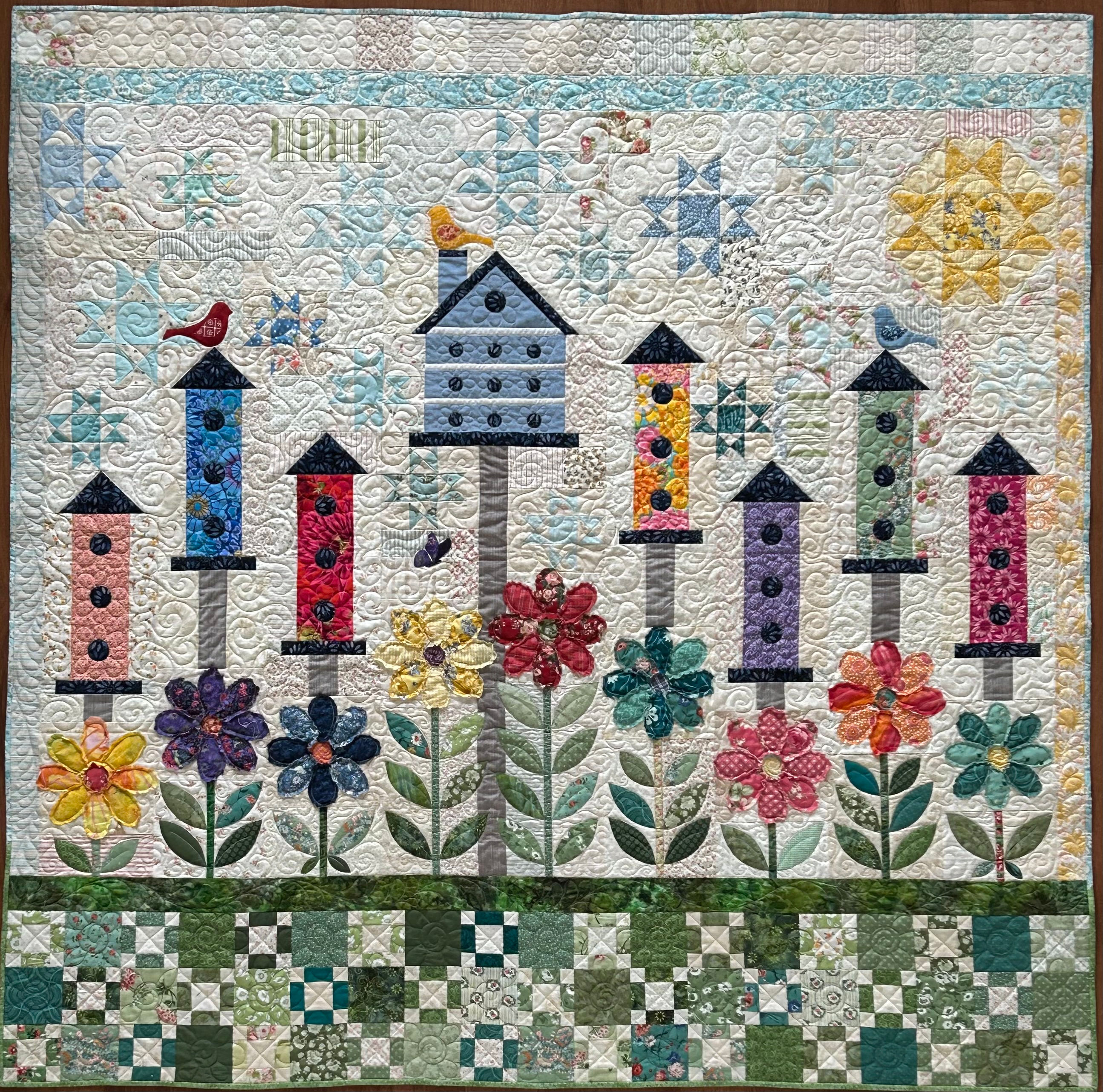 Full view of Morningside, a scrappy birdhouse quilt pattern, features brightly colored bird houses above applique flowers