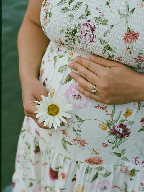 Close-up of pregnant belly in floral maternity dress, warm sunset tones, Lake Ontario film photography