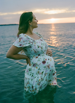 Maternity session portrait, floral dress and windblown hair on Lake Ontario beach