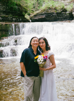 Wide shot of couple in front of Lucifer Falls waterfall on overcast afternoon Finger Lakes engagement