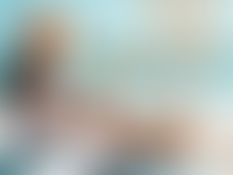 A woman in a sundress and floppy hat holding a popsicle. She is sitting on a beach blanket in the sand with a picnic basket next to her.