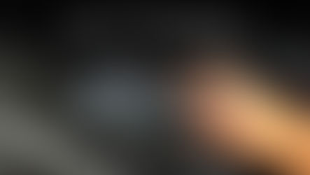 Black car in a garage with a checkered floor. Shelves with cleaning tools line the white walls. Bright, clean, and organized setting.