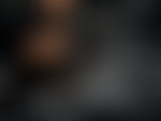 A man in black cap polishing a shiny black car with a buffer in a dimly lit garage. Reflections create dynamic patterns on the car's surface.