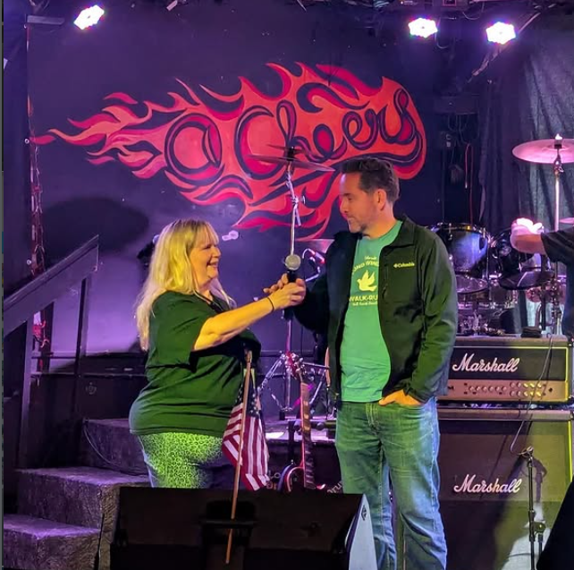 Executive director and Second Wind Fund supporter share the microphone at a benefit concert for suicide loss and prevention