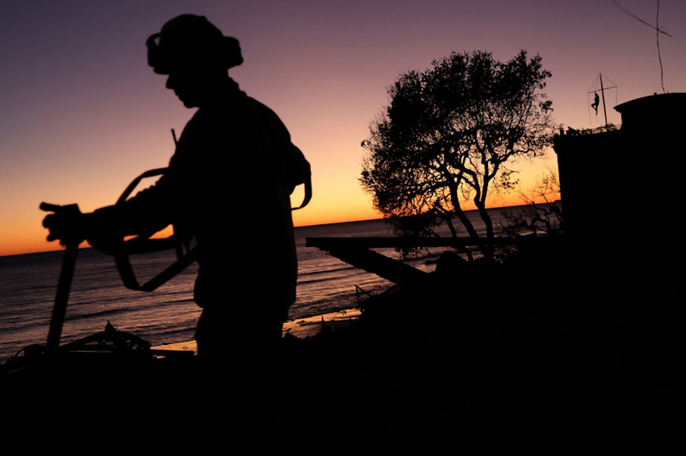 Silhouette of a person holding a tool against an orange-purple sunset by the sea, with trees and a structure in the background. Peaceful mood.