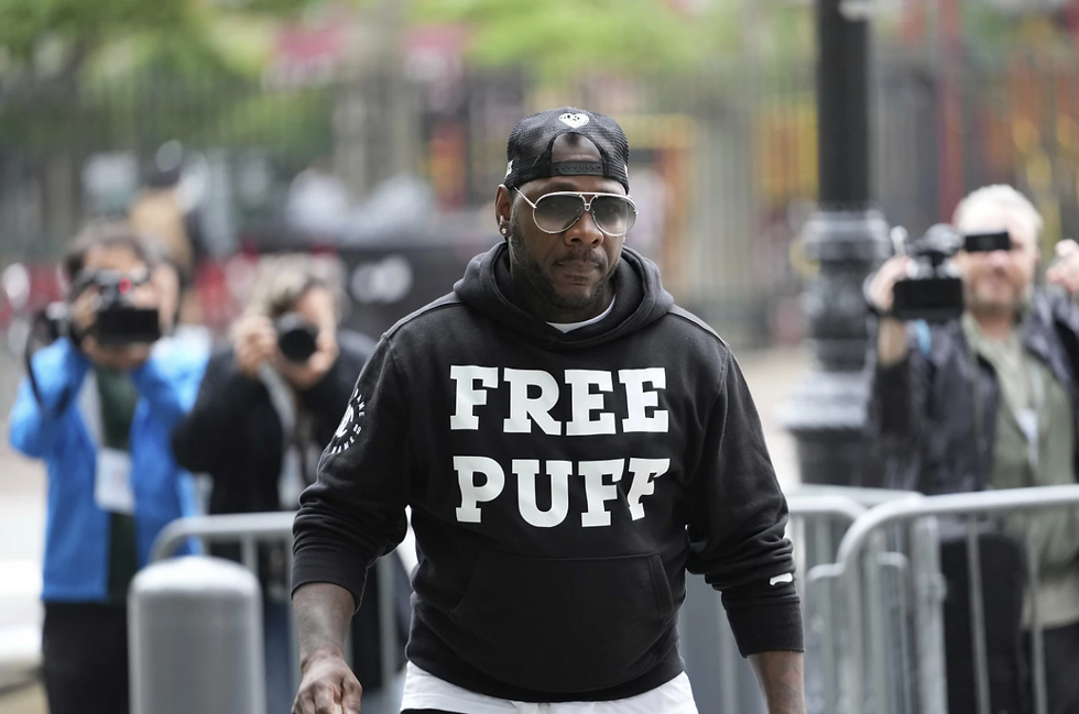 Man wearing "Free Puff" hoodie walks confidently, surrounded by photographers in an outdoor setting with blurred greenery and barriers.