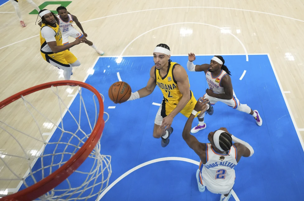 Basketball game: Player in yellow jersey jumps to score, evading defenders in white jerseys on a blue court. Intense action near the hoop.