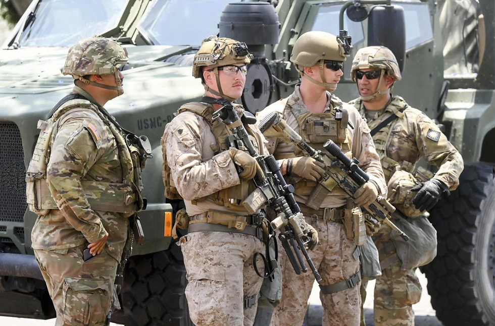 Soldiers in camouflage and gear stand with rifles in front of a military vehicle, displaying focus and readiness in a tactical setting.