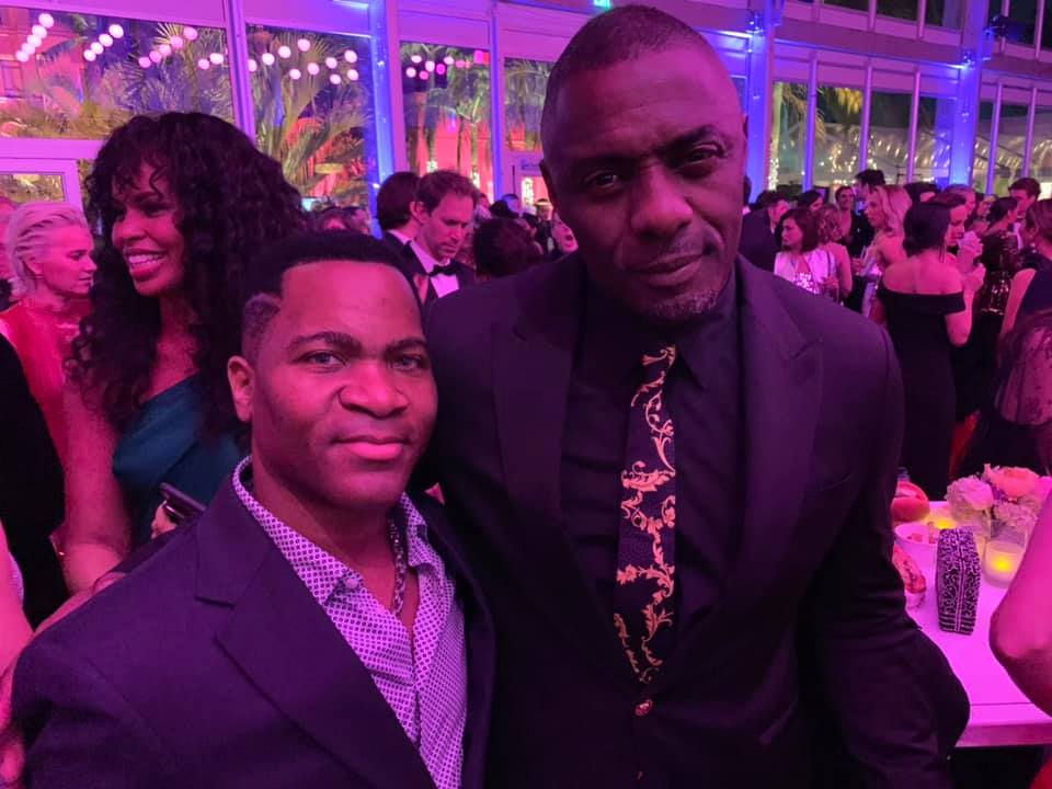 Aaron Bing and Edris Elba pose together at the Vanity Fair Oscar party, with colorful lighting and a stylish crowd in the background.