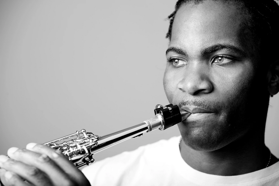 Aaron Bing playing saxophone in black and white image, close-up with focused expression. Plain background, highlighting musical focus.