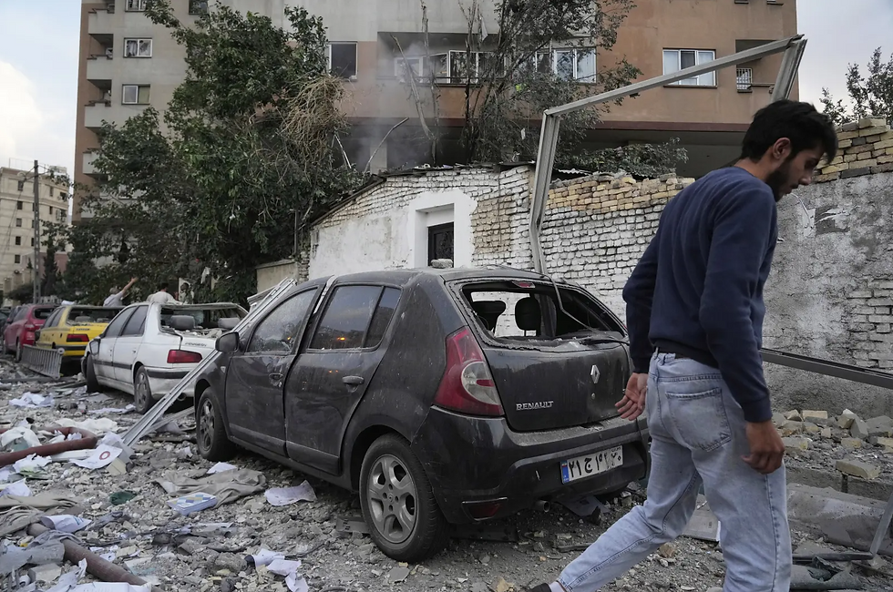 Man walks past a damaged car and debris on a street. Background shows a crumbling wall and building, creating a scene of destruction and chaos.