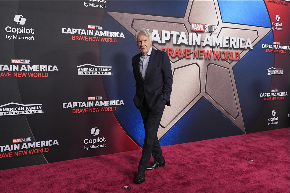 Man in suit on red carpet, posing in front of "Captain America: Brave New World" backdrop. Star design, logos; elegant, professional mood.