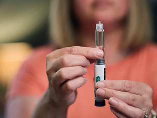 A woman holds a GLP-1 injection pen while demonstrating a smaller dose of weight-loss medication.