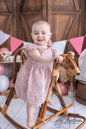 Bébé fille souriant, debout sur cheval à bascule, fond rustique festif.