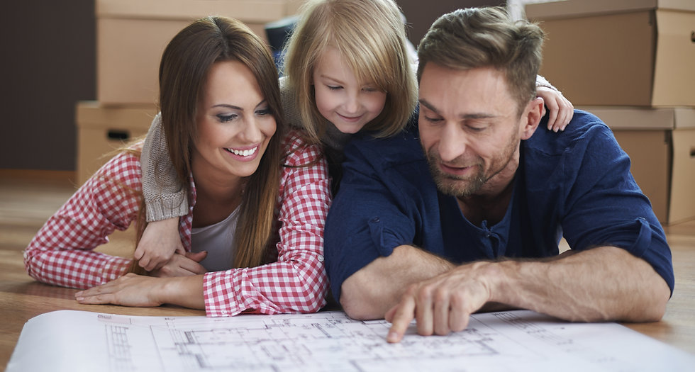Eine Familie mit Mutter, Vater und Tochter schauen sich einen Grundriss einer Wohnung an. Im Hintergrund stehen Umzugskartons.