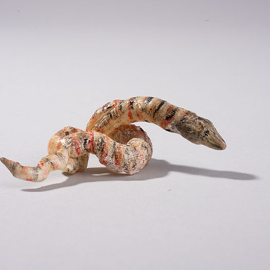Handmade Shellfolk creature shaped like a small curved worm, formed from layered marine materials with a segmented, coiled body and subtle natural colouring.