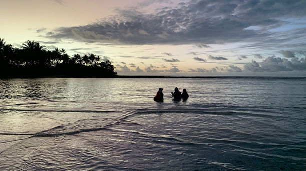 Silhouettes of three people relaxing in the shallow lagoon at sunset, Bokanbotin private island, Marshall Islands