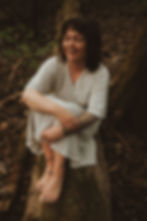 Frau sitzt am Waldboden und lacht, sie fühlt gluck