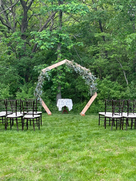 Outdoor wedding ceremony with rustic wooden arch decorated with flowers and geenery