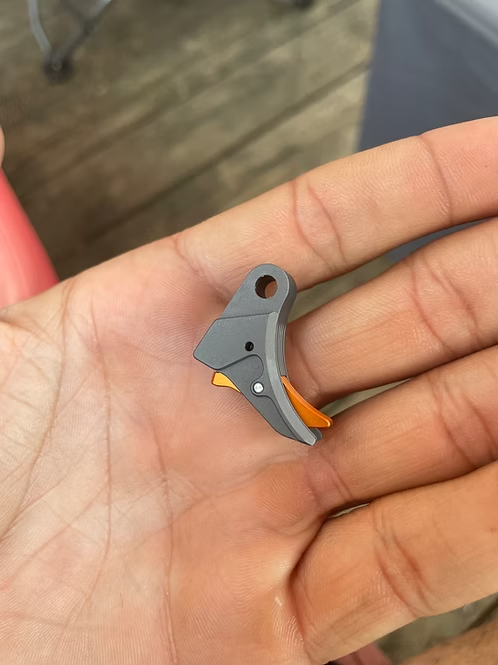 Grey and orange mechanical trigger component held in a person's hand.