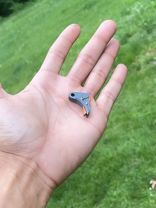 Small gray robotic part held in an open palm outdoors.