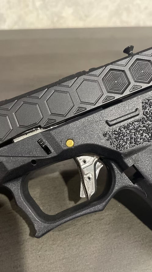 Close-up of firearm with hexagonal slide pattern and stainless steel Vex shoe trigger.