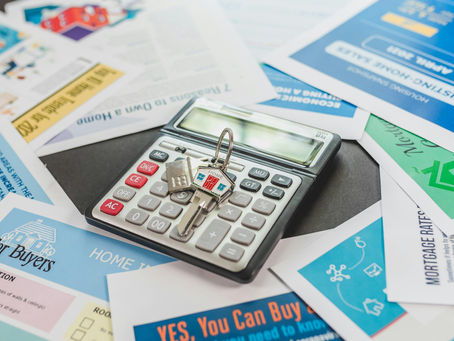 A key on top of a calculator on top of flyers about real estate buyer process.